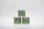 A set of three small glass jars of Tallo Whipped Moisturizer with green labels and white lids, stacked in a pyramid formation. The labels read Unscented. The product is labeled as handmade, organic, and made with grass-fed tallow.
