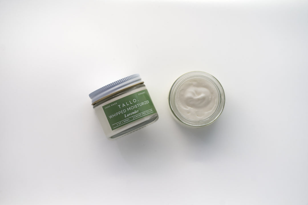 Two glass jars of Tallo Whipped Moisturizer with green labels and white lids, placed side by side. One jar is labeled 'Lavender,' while the other features a different variation. The labels indicate that the product is handmade, organic, and made from grass-fed tallow