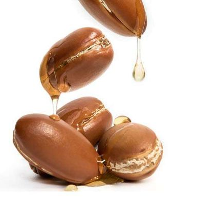 Close-up of jojoba seeds with golden jojoba oil dripping from them against a white background. The oil flows from the cracked seeds, highlighting its rich and nourishing texture.