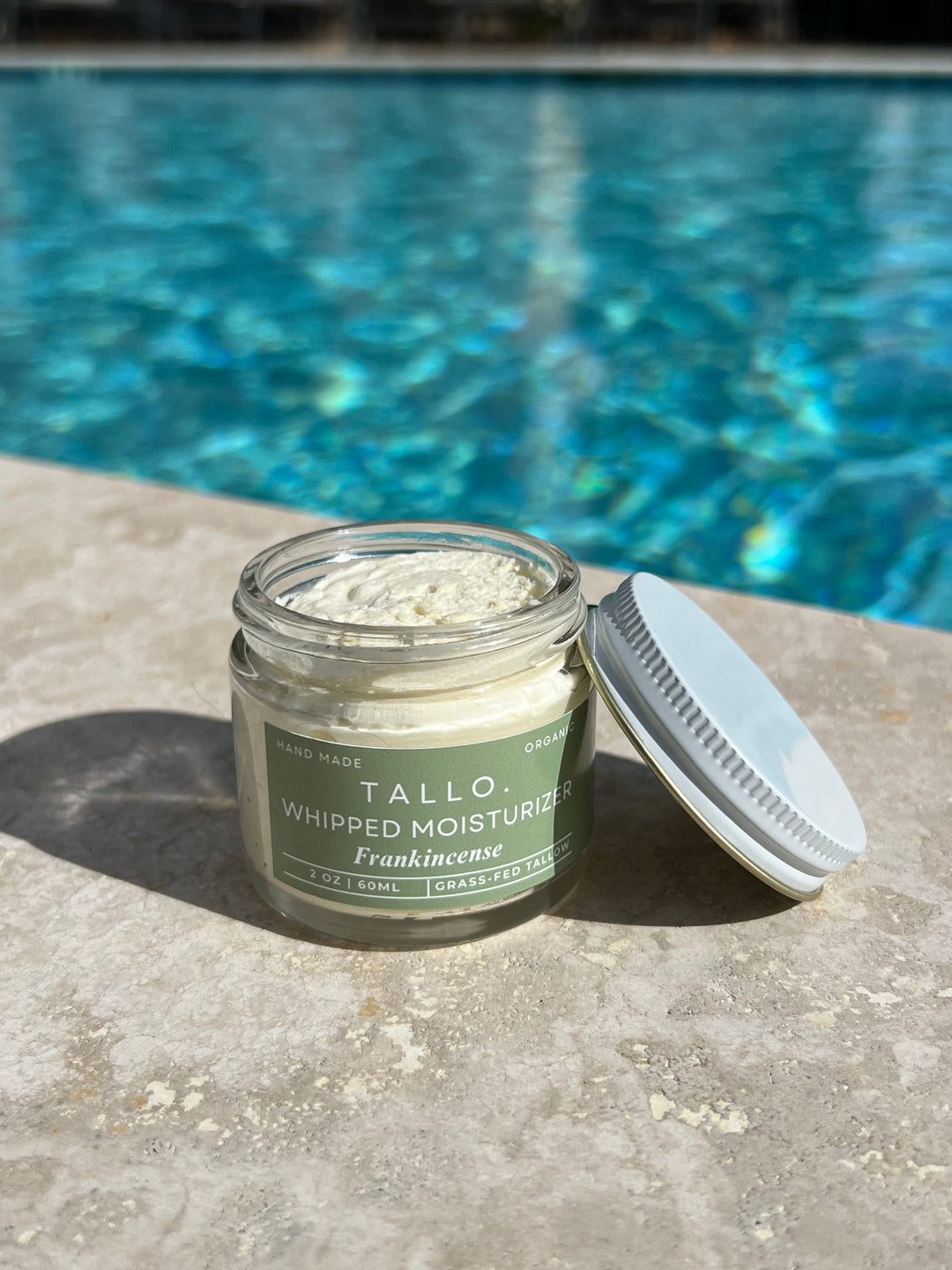 Frankincense Tallo Skincare 2 oz jar with the lid leaning on the jar. Nourishing and hydrating skincare item with a white lotion texture