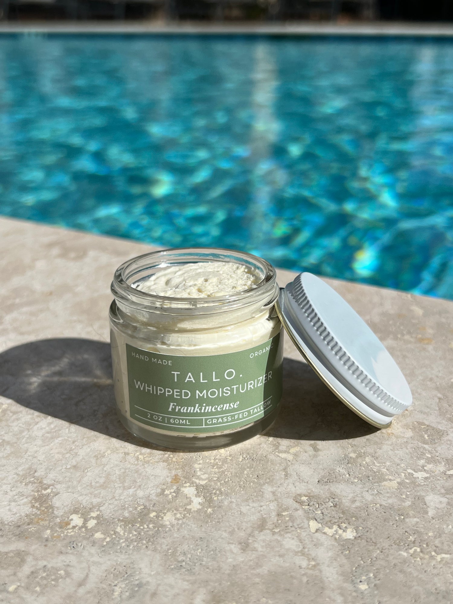 Frankincense Tallo Skincare 2 oz jar with the lid leaning on the jar. Nourishing and hydrating skincare item with a white lotion texture