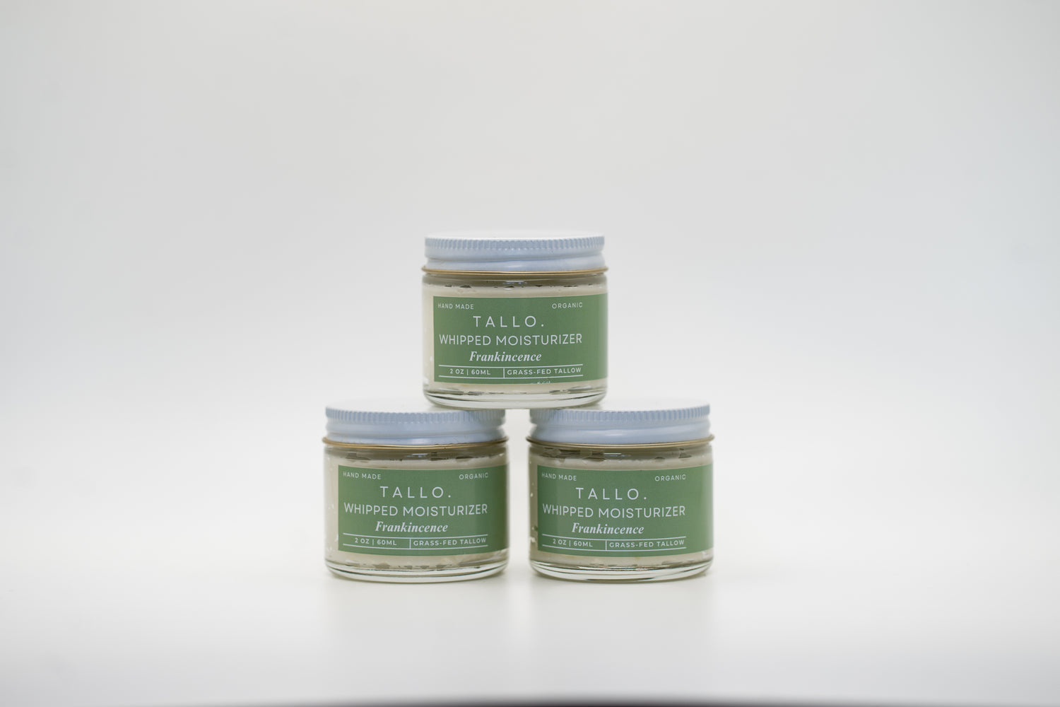 A set of three small glass jars of Tallo Whipped Moisturizer with green labels and white lids, stacked in a pyramid formation. The labels read Frankincense. The product is labeled as handmade, organic, and made with grass-fed tallow.