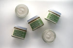 five glass jars of Tallo Whipped Moisturizer with green labels and white lids, spread out on a white background. Each jar features a different scent: Frankincense, Lavender, and Unscented. The labels highlight that the product is handmade, organic, and made from grass-fed tallow.