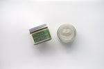 Two glass jars of Tallo Whipped Moisturizer with green labels and white lids, placed side by side. One jar is labeled 'Frankincense,' while the other features a different variation. The labels indicate that the product is handmade, organic, and made from grass-fed tallow.