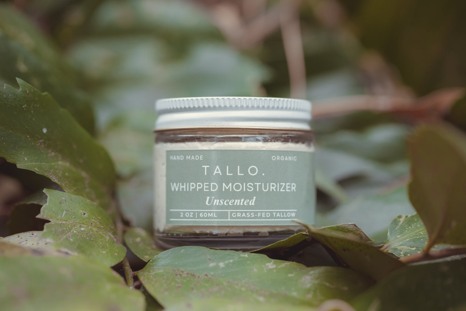 2 oz glass jar of Tallo Whipped Moisturizer unscented with a green label and a white jar. Green leaves are hold up the hydrating, moisturizing skincare.