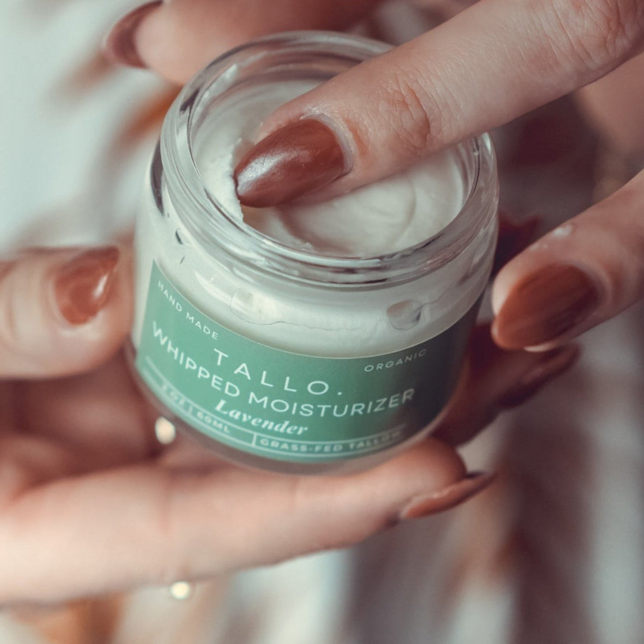 2 oz glass jar of Tallo Whipped Moistuzier with a green label. Label describes the grass-fed beef tallow used in the skincare along with other organic ingredients.